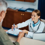 Imagem mostra uma médica e um paciente. A doutora está dando orientações sobre reembolso médico para a pessoa durante o atendimento.